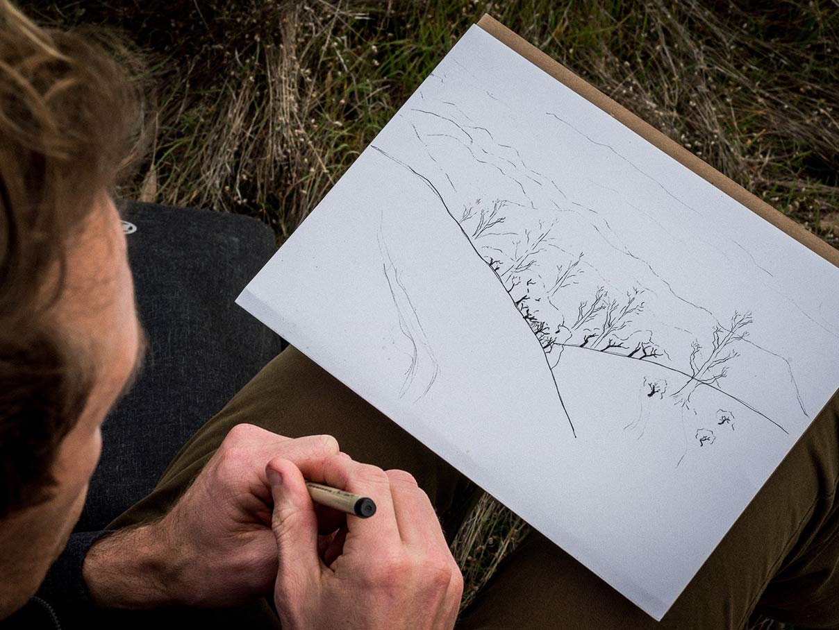man sketching outdoors using a technical pen and s